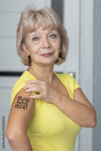 A woman with a tattoo with a QR code of vaccination on her shoulder on a light background. Concept: assignment of a QR code, people with antibodies to the virus, vaccination against coronavirus, antig photo