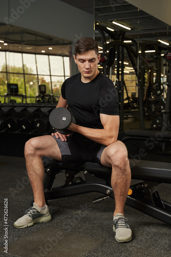 young man shakes biceps with a dumbbell in the gym