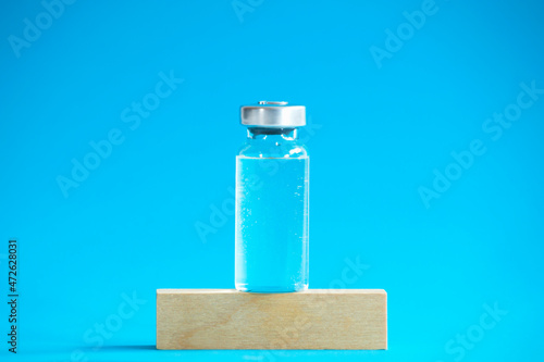 Glass vaccine bottle stands on a wooden cube.