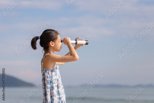 Happy kid playing outdoors on the beach, Asian child girl looking in spyglass photo