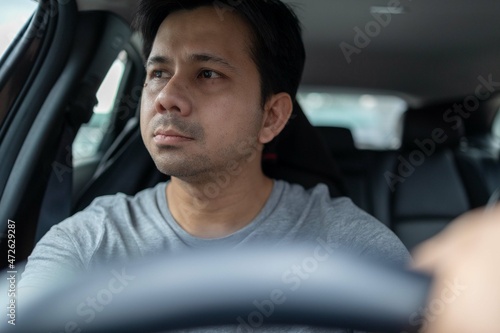 Asian man driving a car looking to the side of the road