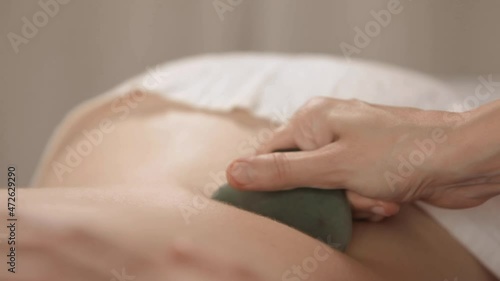 Massage session: woman receiving back Guasha from professional masseur. Attractive caucasian woman having relaxing massage on the back in spa salon. Healthy lifestyle and body care concept