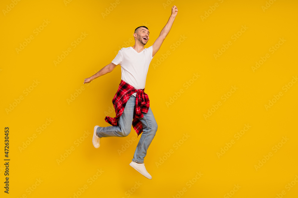 Full body photo of young dreamy man jump up raise hand super hero checkered shirt tied on waist isolated on yellow color background