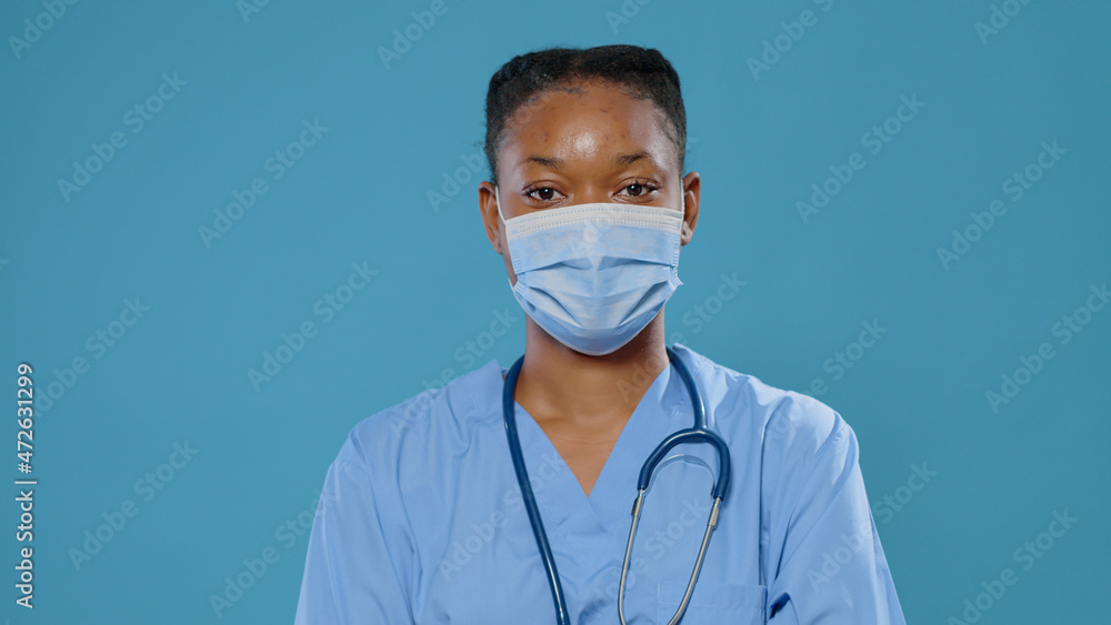 Close up of african american nurse smiling at camera. Portrait of medical assistant wearing face mask for protection against coronavirus while wearing uniform and stethoscope in studio. Close up of african american nurse smiling at camera. Portrait of medical assistant wearing face mask for protection against coronavirus while wearing uniform and stethoscope in studio.