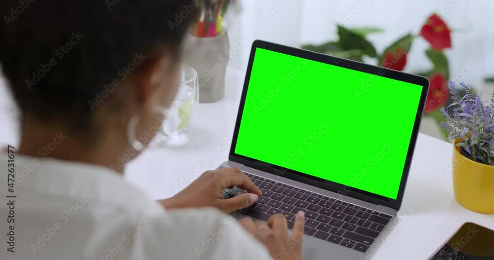 Over the Shoulder Shot of African American Business Woman Typing on Laptop, Young Female Professional Writing an Important Email From Her Home in Modern Living Room. Remote Working. Green Screen. Over the Shoulder Shot of African American Business Woman Typing on Laptop, Young Female Professional Writing an Important Email From Her Home in Modern Living Room. Remote Working. Green Screen.