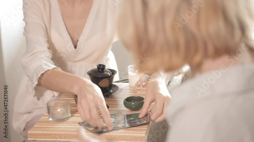 Counselor showing metaphorical cards. Two women are drinking tea while conducting a Chinese tea ceremony. A woman reading a future by tarot cards. Esoteric concept, fortune-telling, and predictions.