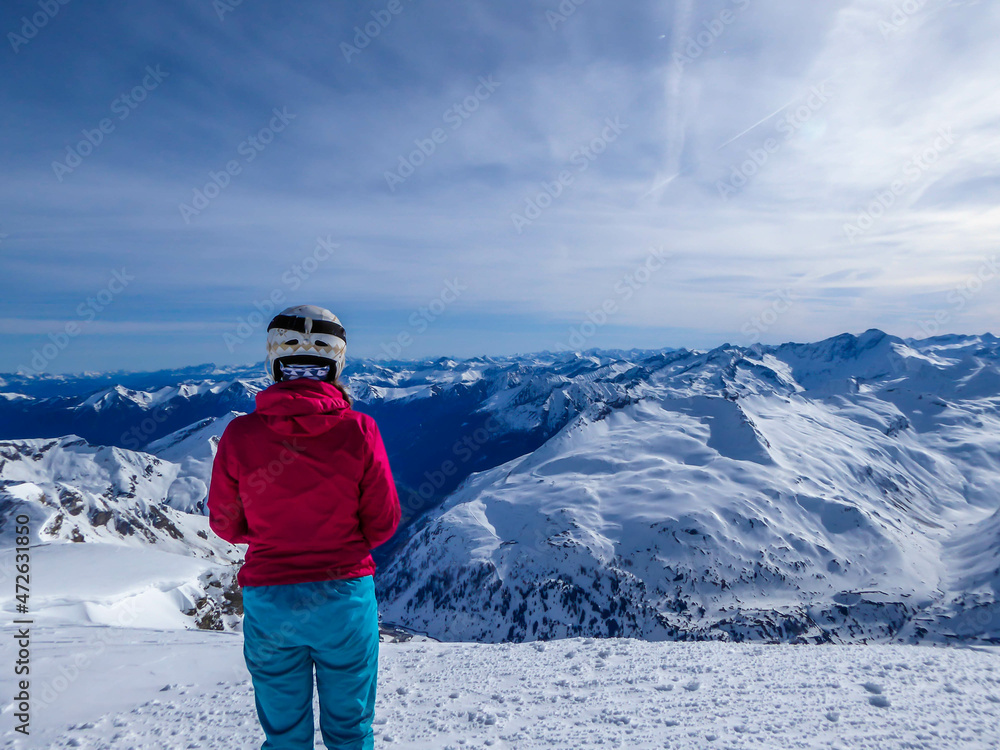 Snowboarding girl standing on the top of a mountain in Moelltaler Gletscher, Austria, enjoying the view. Lots of snow in the mountains. Endless Alps chain. Winter wonderland. Calmness and happiness.