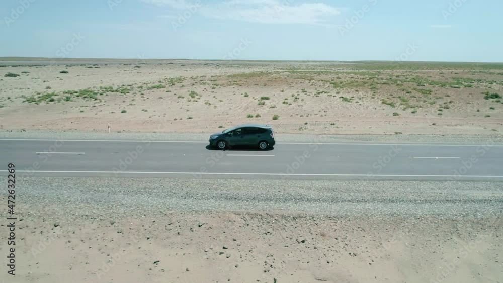 Aerial side view of a car driving on a highway road between sands with little green grass bushes. Aerial side view of a car driving on a highway road between sands with little green grass bushes.
