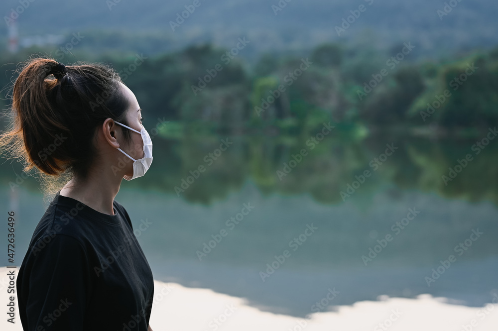 Side view point of young woman wear protection mask beside the lake and her look at faraway , hope and dream concept Side view point of young woman wear protection mask beside the lake and her look at faraway , hope and dream concept