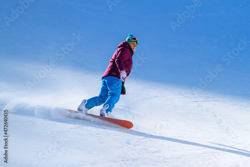 Girl snowboarder slides down the slope on a board throwing snow to the sides. Lone snowboarder on the ski slope. Active recreation during the winter vacations.