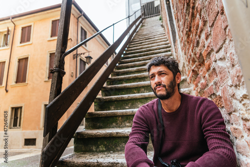 Fotografia A young homeless Latino immigrant rests bored on the steps of an old European city