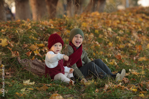 brother and sister are sitting together and laughing, the boy is wearing a green knitted hat, a green sweater, a red scarf, and the girl is wearing a white knitted sweater, a red sundress, a red hat a
