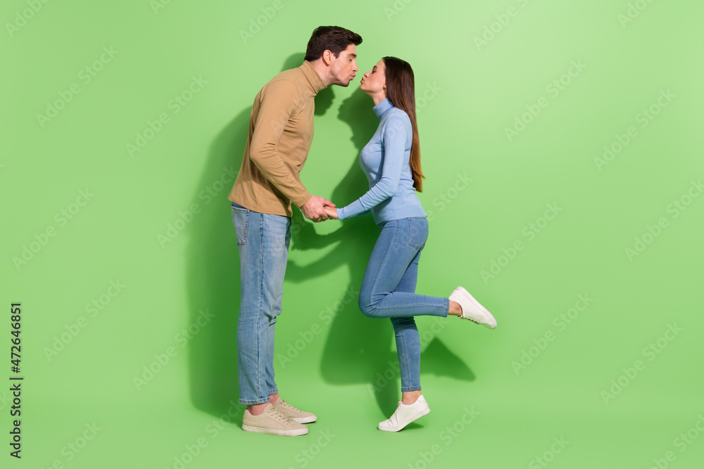 Full size profile portrait of two lovely idyllic persons hold arms kiss lips isolated on green color background Full size profile portrait of two lovely idyllic persons hold arms kiss lips isolated on green color background