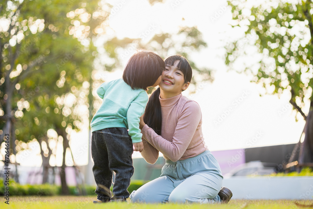 Fototapeta premium Happy asian family mother and kid spending time together at the park. Kissing each other. Have fun enjoy family time at weekend with beautiful sun light. Lifestyle Childhood and weekend concept