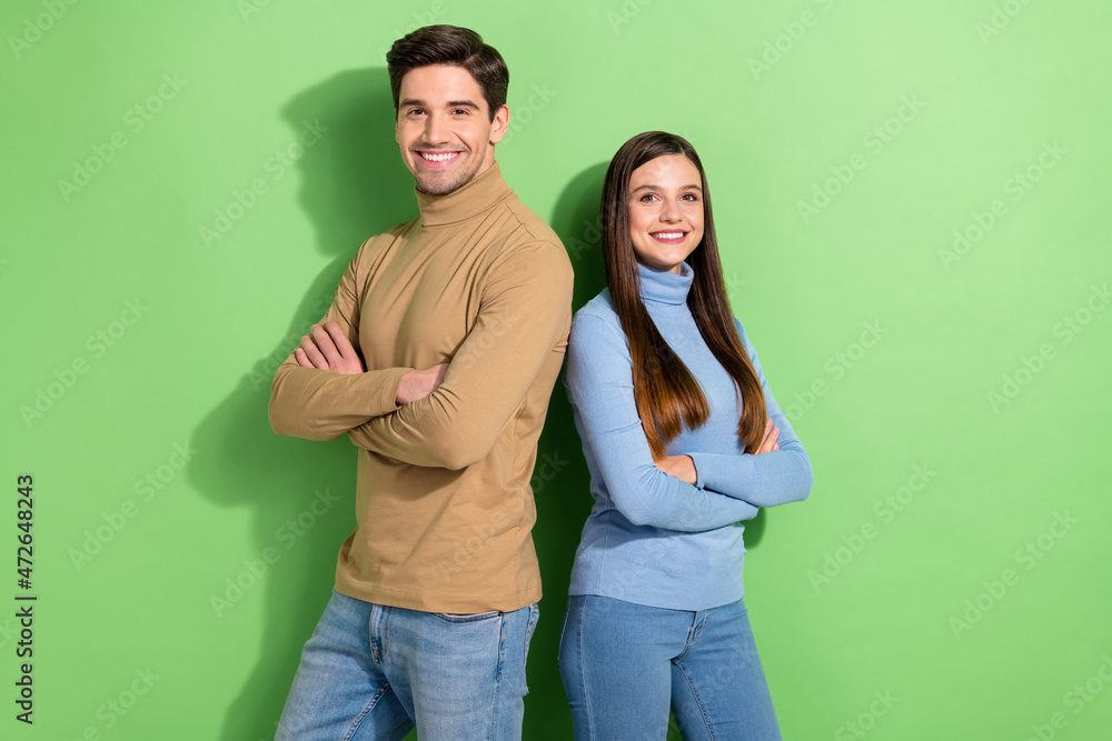 Fototapeta premium Portrait of two positive attractive people stand back to back crossed arms isolated on green color background