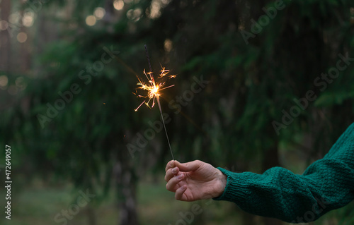 Sparkler firework in women's hand in forest. Christmas holidays celebration concept greeting card 