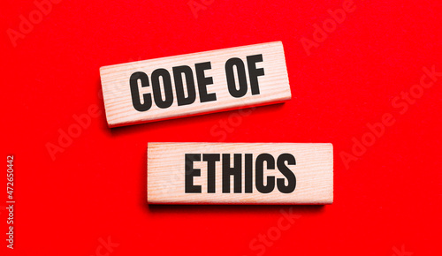 On a bright red background, there are two light wooden blocks with the text CODE OF ETHICS