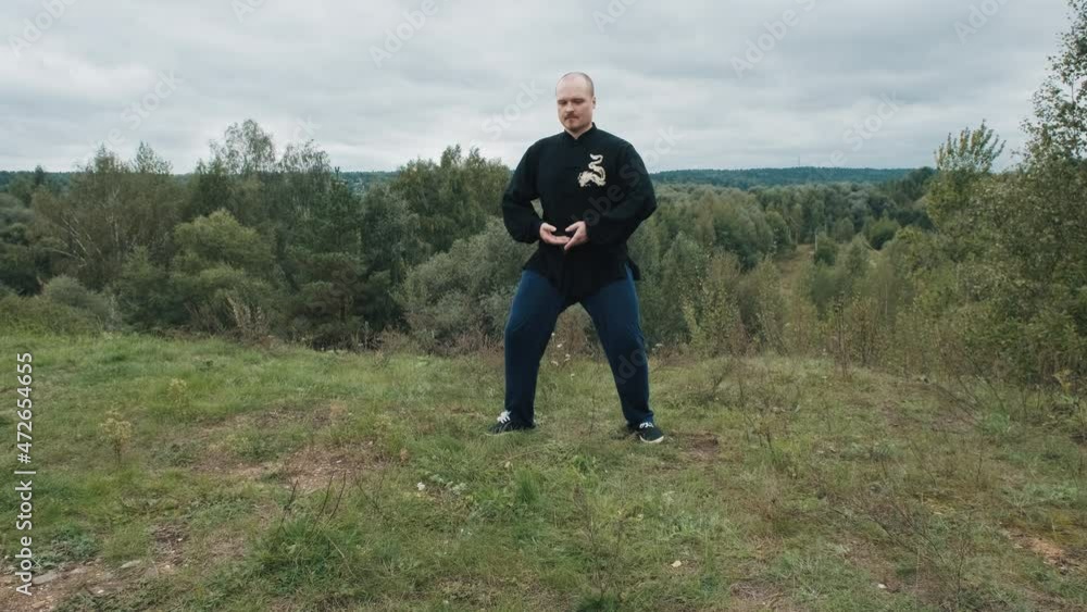 Middle aged Caucasian man practices wushu in the summer in a park on a hill. Traditional Chinese gymnastics qigong and Tai chi. Meditation and relaxation in nature. Healthy lifestyle and sports Middle aged Caucasian man practices wushu in the summer in a park on a hill. Traditional Chinese gymnastics qigong and Tai chi. Meditation and relaxation in nature. Healthy lifestyle and sports