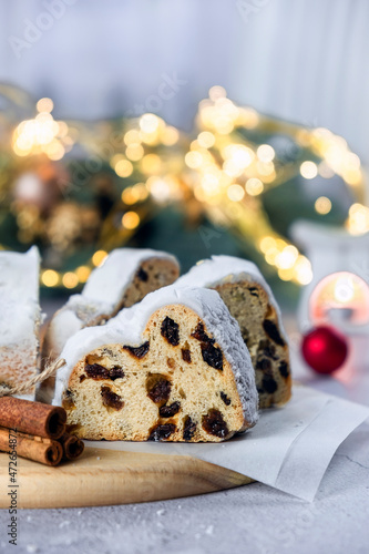 German Stollen cake, traditional European dessert with dried fruit, raisins, nuts and marzipan. Christmas pie with cinnamon and Christmas lights on background. Recipe of homemade dessert for holidays. photo