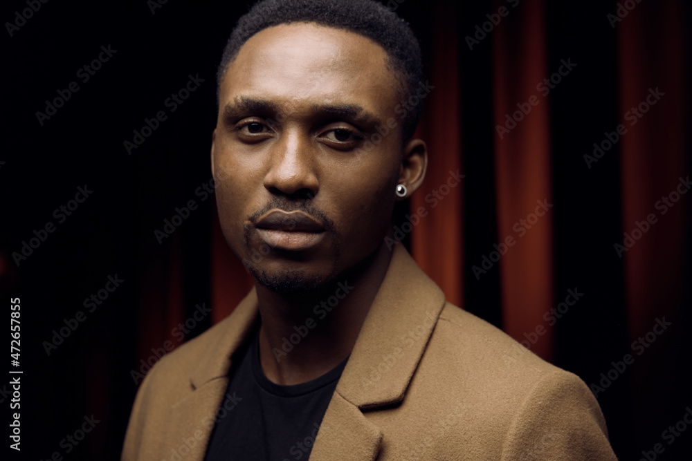 Obraz premium Black man. Dressed in a brown coat. Looking straight into the camera. In his ear he has a silver bead
