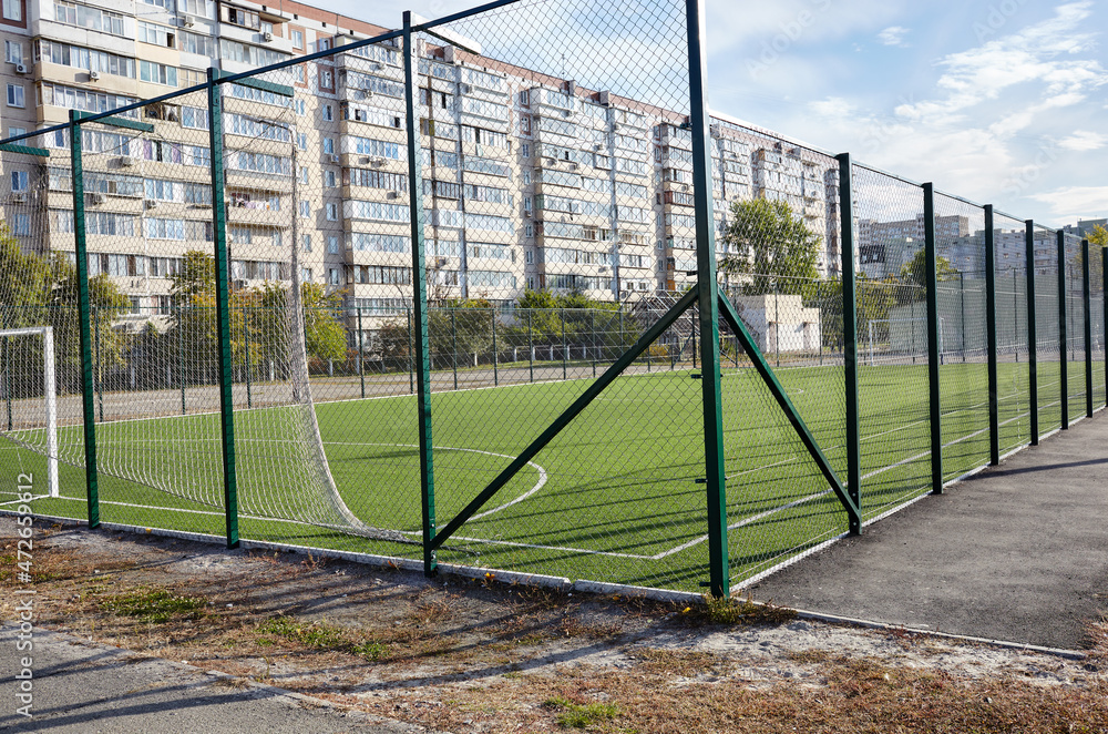 Fototapeta premium Lawn field for playing football behind the green fence mesh. Close-up of soccer field with green grass