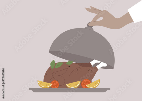 A waiter opening a metal cloche, a roasted chicken served with herbs and vegetables on a tray