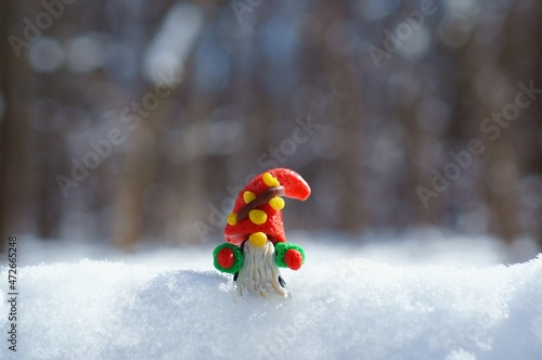 A figurine of a dwarf made of plasticine in a snowy forest. A fairy-tale character.