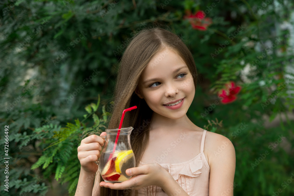 Cute little girl drinks lemonade front of green leaves background. Kid holds glass with summer beverage cold tea. Copyspace Cute little girl drinks lemonade front of green leaves background. Kid holds glass with summer beverage cold tea. Copyspace