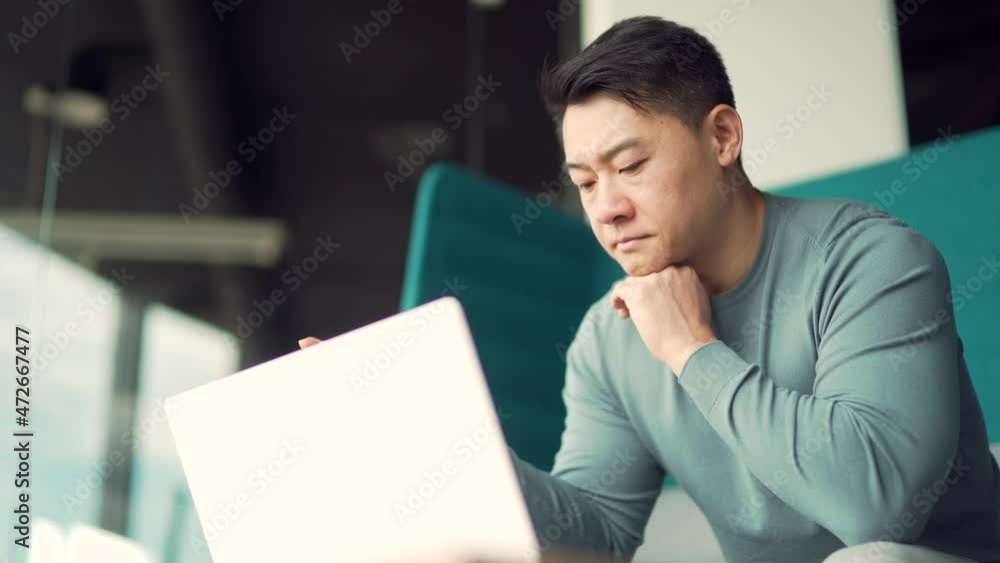 Portrait thoughtful young Asian freelancer working on a laptop computer at a modern office desk. Confident Focused pensive man entrepreneur indoors. thinking of inspiration solving a problem. Startup Portrait thoughtful young Asian freelancer working on a laptop computer at a modern office desk. Confident Focused pensive man entrepreneur indoors. thinking of inspiration solving a problem. Startup