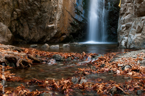 Waterfall and river flowing with maple leaves on the rocks on the river in Autumn