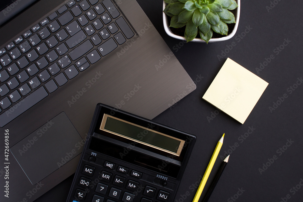 Top view of office desk with laptop, calculator and pencil on the black background. Close-up. Flat lay of workspace desk. Top view of office desk with laptop, calculator and pencil on the black background. Close-up. Flat lay of workspace desk.