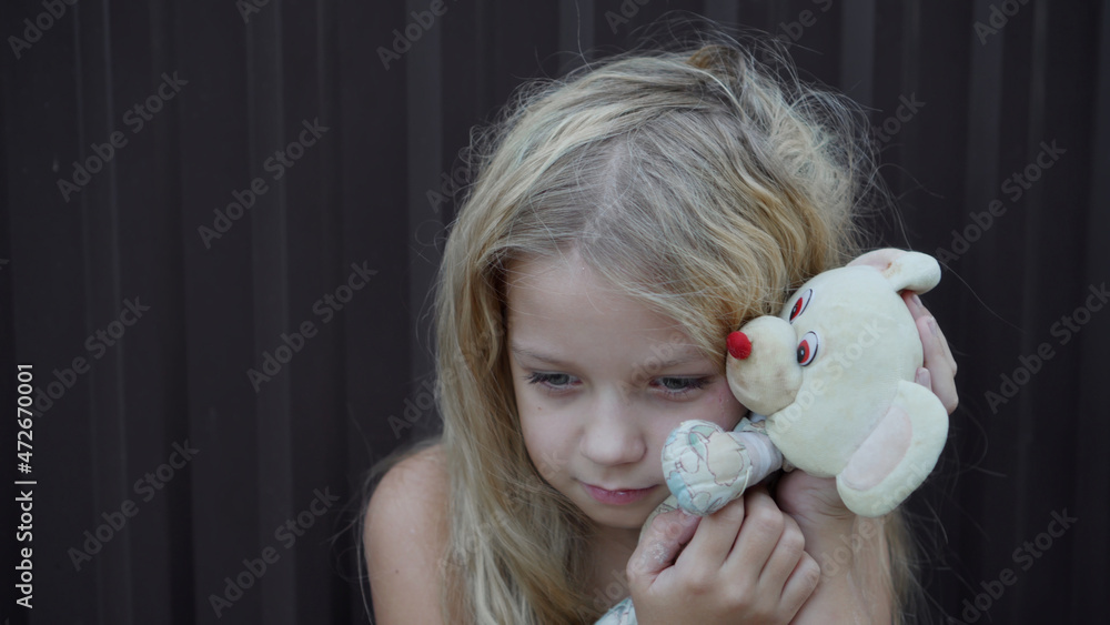 The poor girl with disheveled hair tenderly hugs her favorite simple toy. The poor girl with disheveled hair tenderly hugs her favorite simple toy.