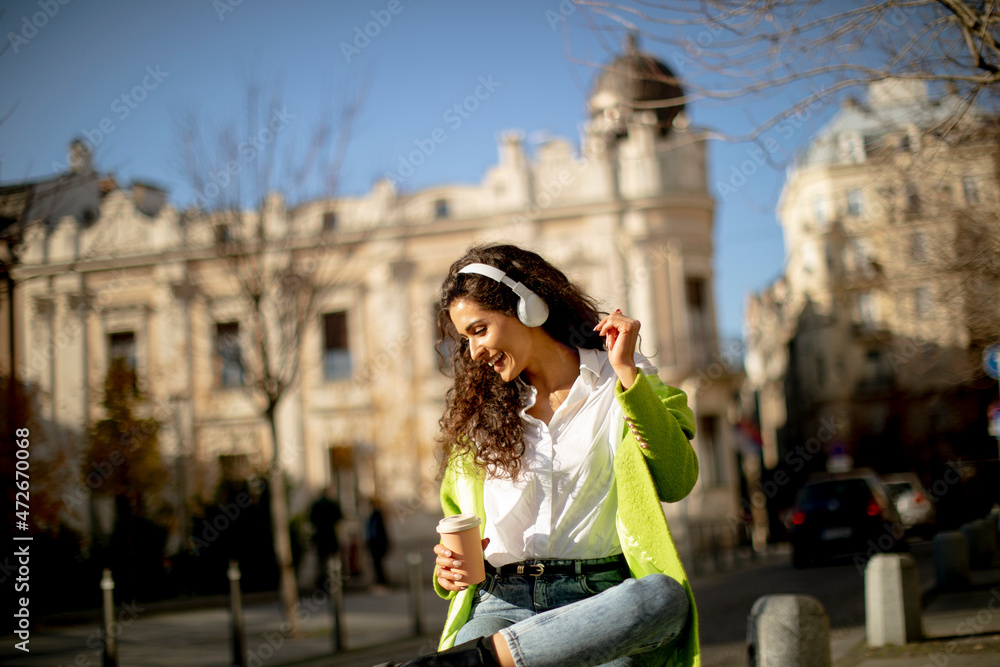 Young woman listening music with smartphone on the street and holding takeaway coffee
