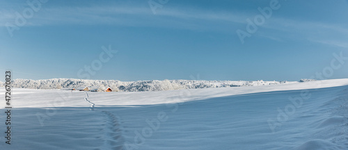 Fußspur über ein verschneites Feld zu einem Bauernhaus