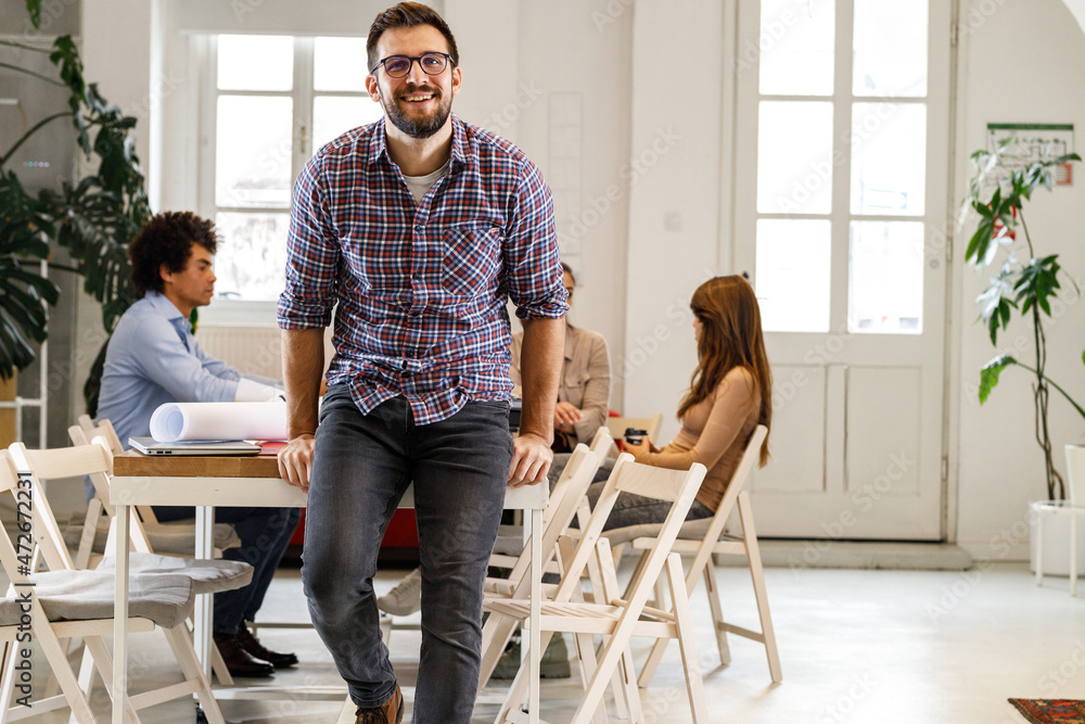 Fototapeta premium Portrait of casually dressed businessman sitting on desk in his office.