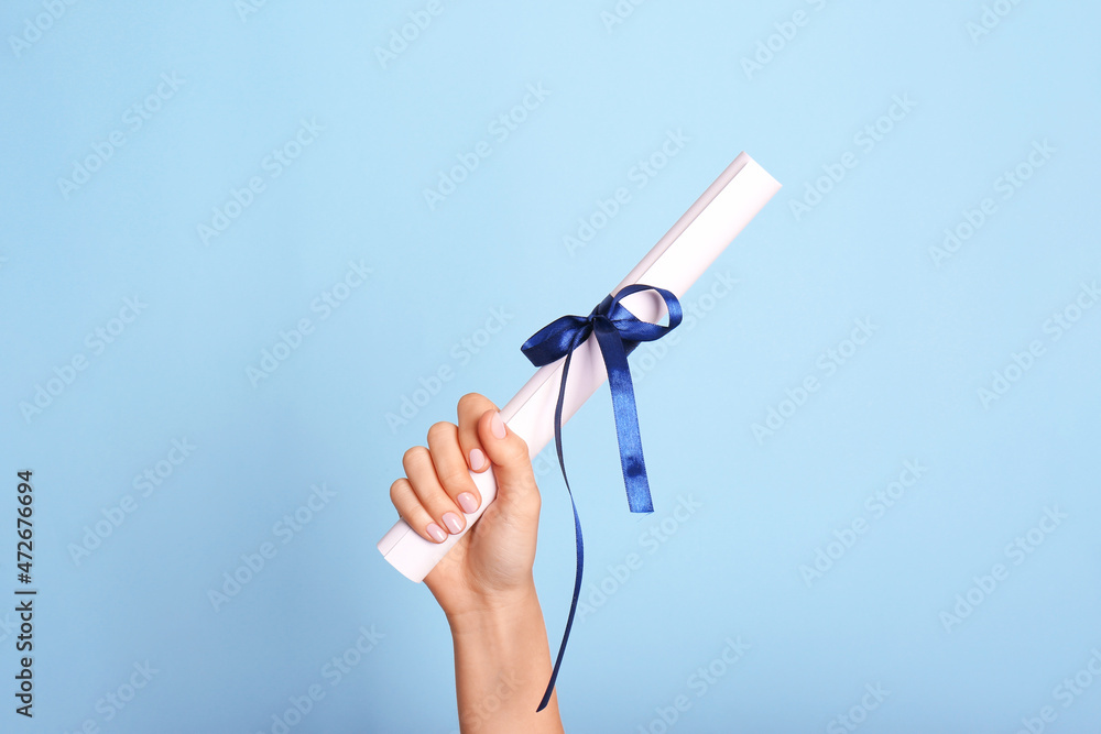Student holding rolled diploma with ribbon on light blue background, closeup - obrazy, fototapety, plakaty 
