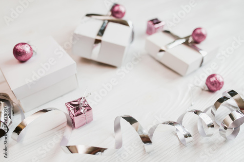 Gifts in white boxes with silver wrapping ribbons and pacific pink Christmas balls on a light wooden table