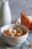 pumpkin cream soup with croutons, pumpkin seeds in a white bowl, milk bottle and pumpkin  on a light background