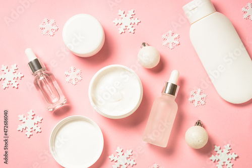 Winter cosmetic, skin care product. Cream, serum, tonic with winter decorations. Top view on pink background with copy space.