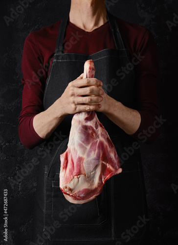 Butcher holds raw lamb leg in hands over black background