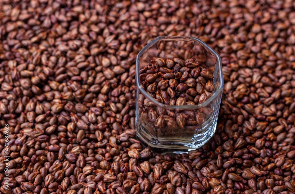 A small glass with dried grape seeds on the background of their scattering