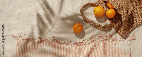 Fresh oranges falling out from woven bag on sandy beach. Linen beach towel with fringes detail. Tropical holidays concept