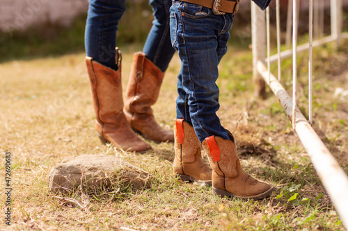 Legs of two people in jeans and cowboy boots on a ranch