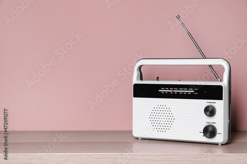 Retro radio receiver on wooden table against pink background. Space for text
