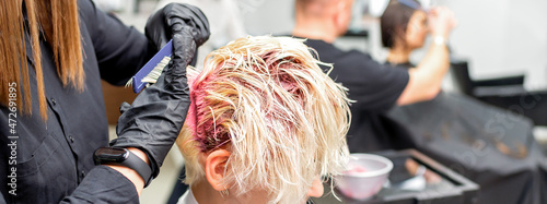 The professional hairdresser uses a brush to apply the pink dye to the hair. Hair coloring concept