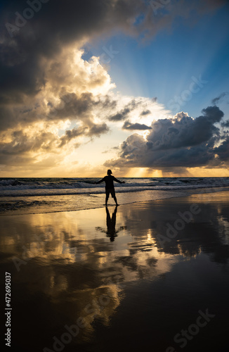 Silhouette of a young age man standing on the edge of the sea during sunrise.