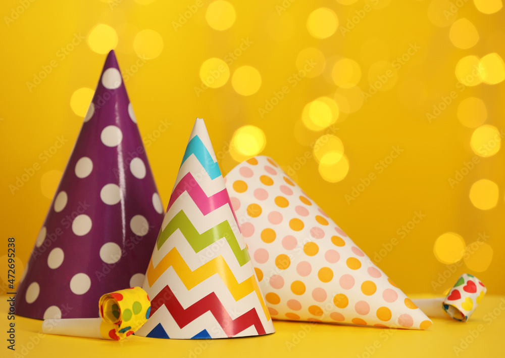 Beautiful party hats and blowers on yellow table against blurred festive lights. Space for text
