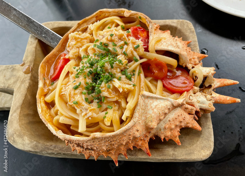 Fresh spider crab pasta served in its shell on wooden plate.