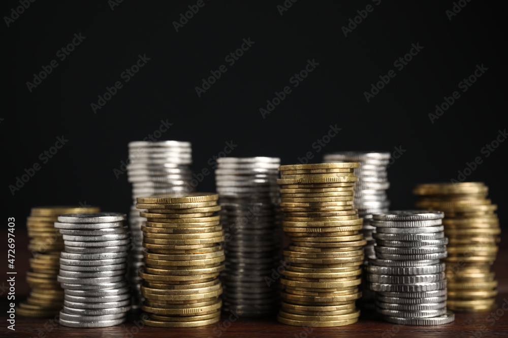 Many coins stacked on wooden table against black background Many coins stacked on wooden table against black background