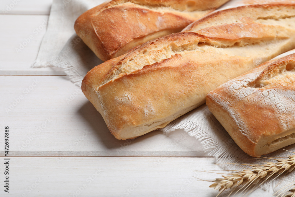 Tasty baguettes and spikelets on white wooden table, closeup